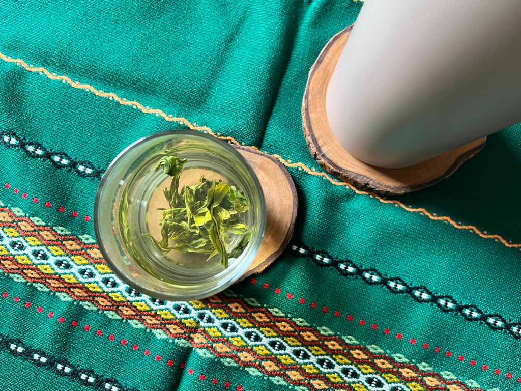 A glass of grandpa-style green tea next to a thermos on a green patterned cloth
