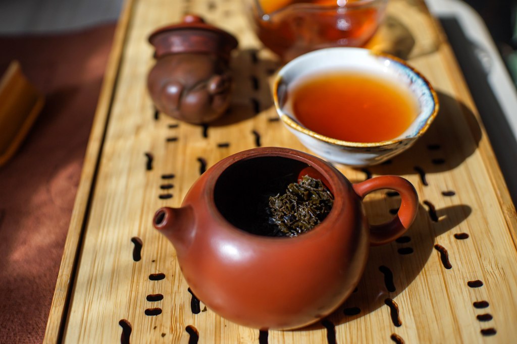 Open clay pot containing Koji Plum leaf in the foreground, with cup and pig teapet in the background