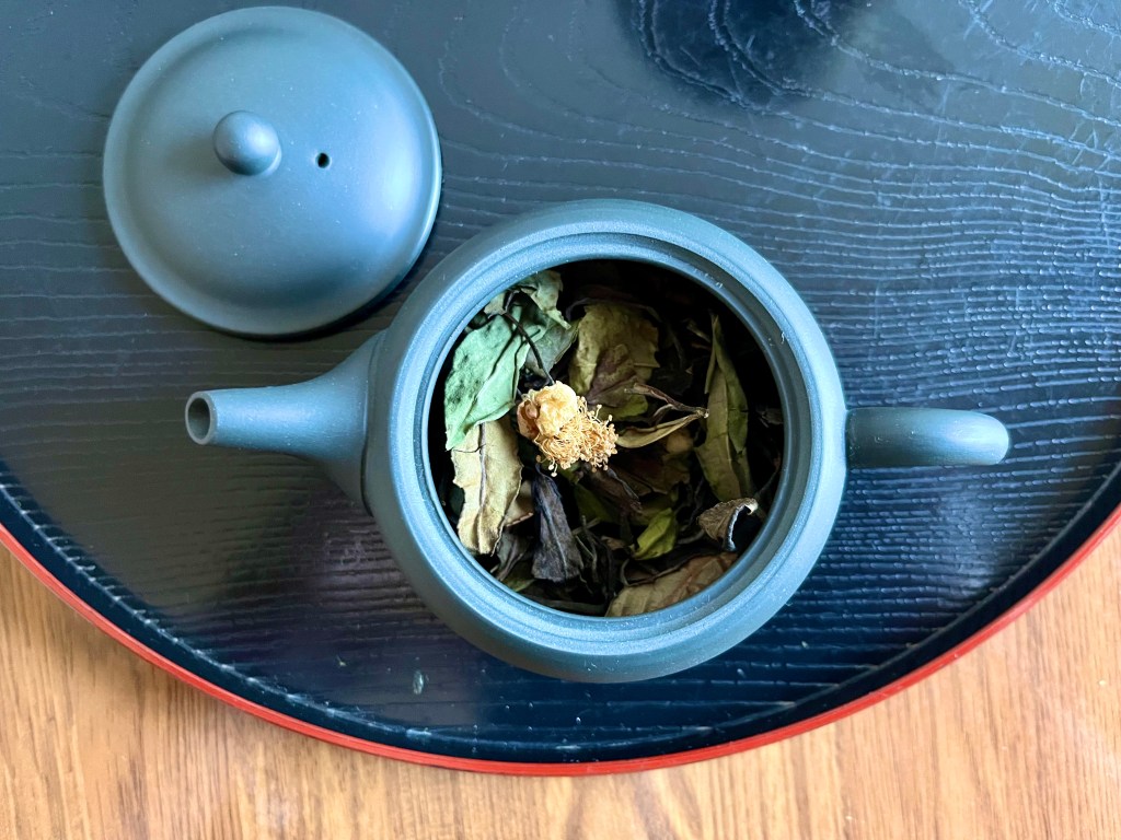 Small black clay pot on a black tray with white tea and tea flowers inside