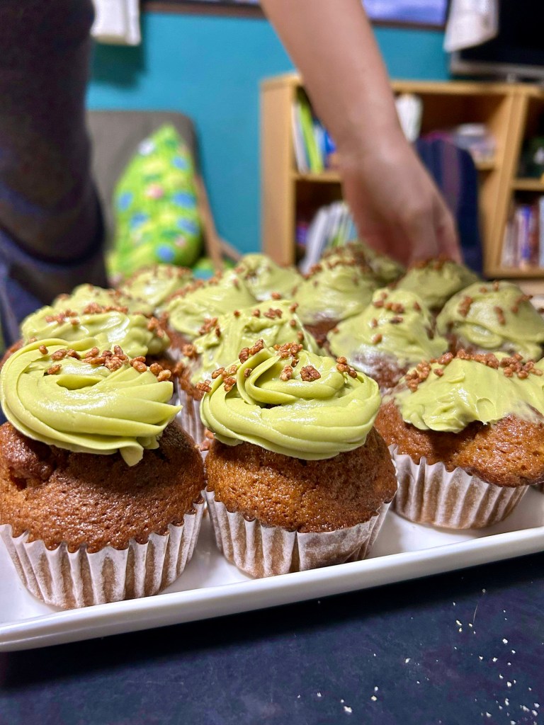 Close-up of two beautifully frosted cupcakes, with the rest in the background looking a bit of a mess