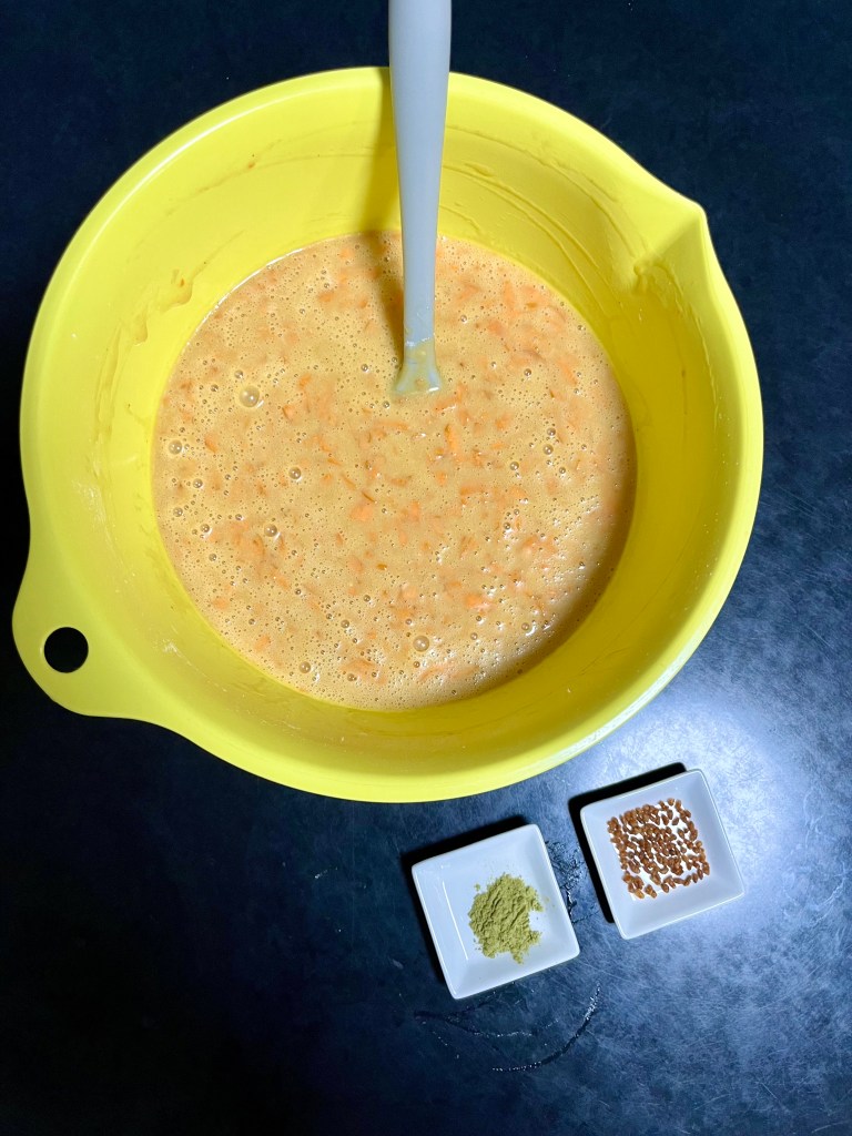 Finished carrot cupcake batter in a yellow bowl, with trays of genmai and genmaicha powder