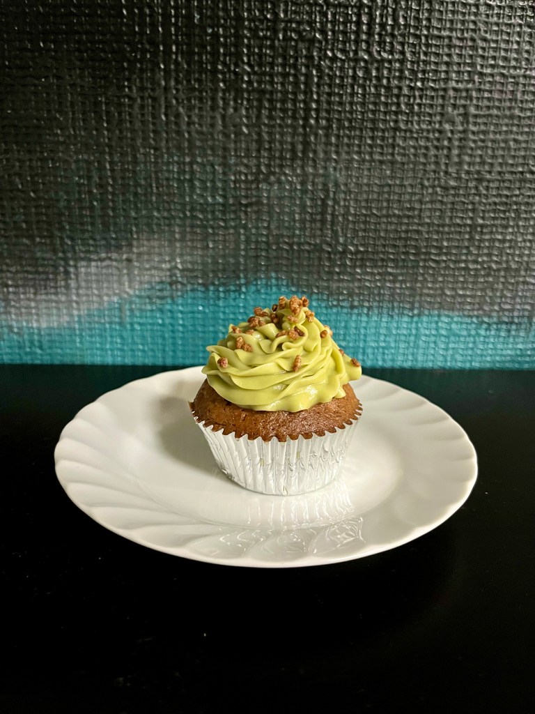 One carrot cupcake with genmaicha frosting in a silver cupcake liner on a white plate