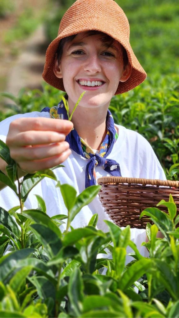 Maren at Monzen, holding up two leaves and a bud and smiling at the camera