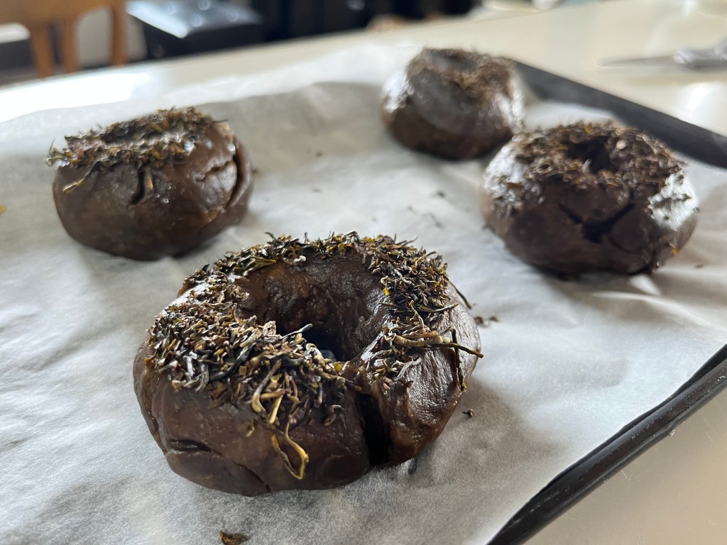 Black tea bagels on a baking sheet: they're dark brown in colour and topped with the roasted broken tea pieces